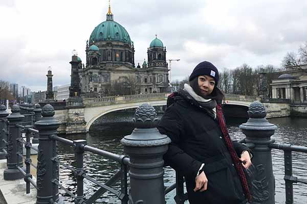 student in winter hat and coat posing in Berlin with building architecture of location in background on water