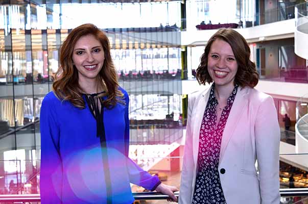 two female students in suits posing with blurred glass interior building in background