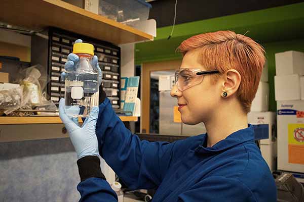 student in blue lab coat looking at chemical in bottle in lab