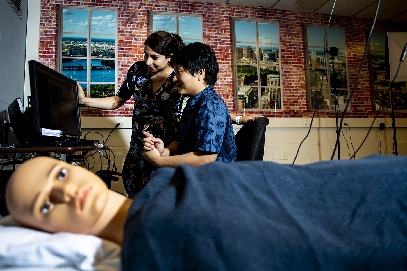 professor and researcher looking at monitor with manikin in bed