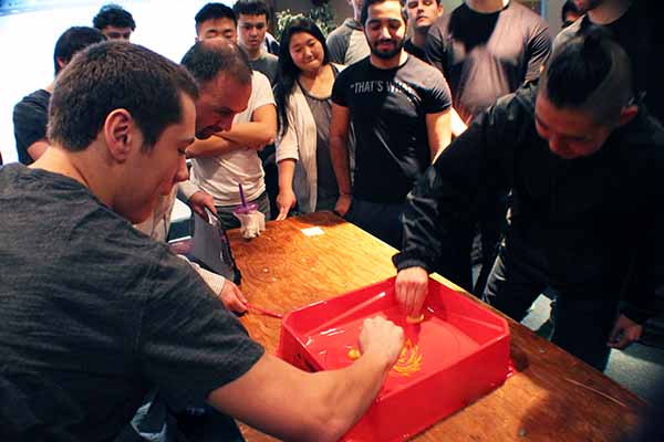group looking at two students with red container on table working together