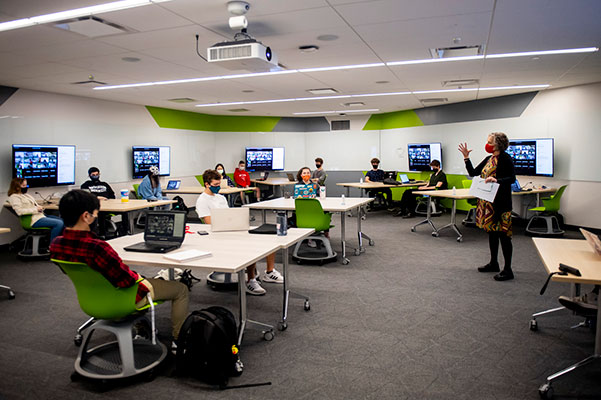 professor in classroom with students at tables with masks on