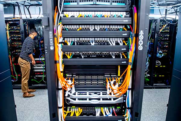 plugging network cables into the back of servers in big Colosseum data center
