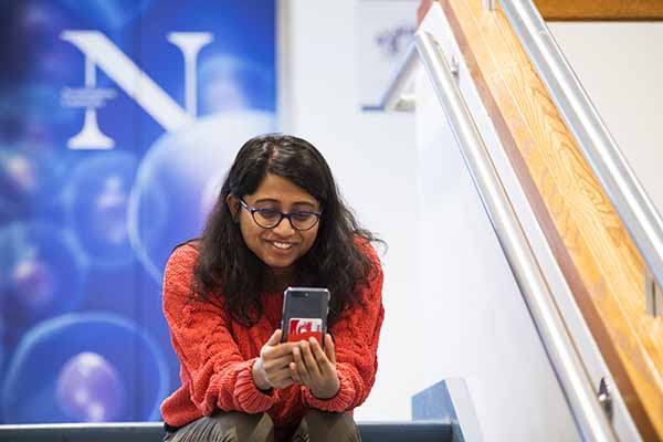 student sitting on stairs with the N logo in background and looking and smiling at mobile phone